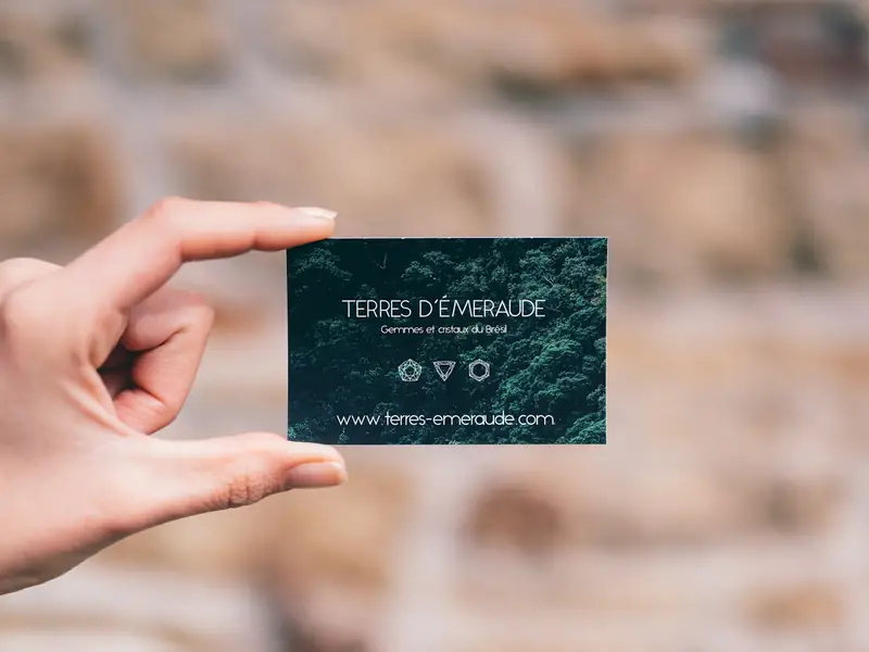 A hand holding a dark green business card