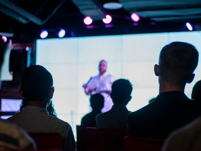 A speaker on stage in front of a large screen