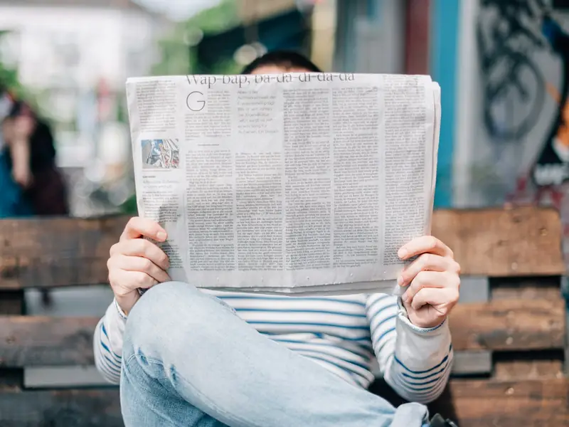A man reading a newspaper on a bench